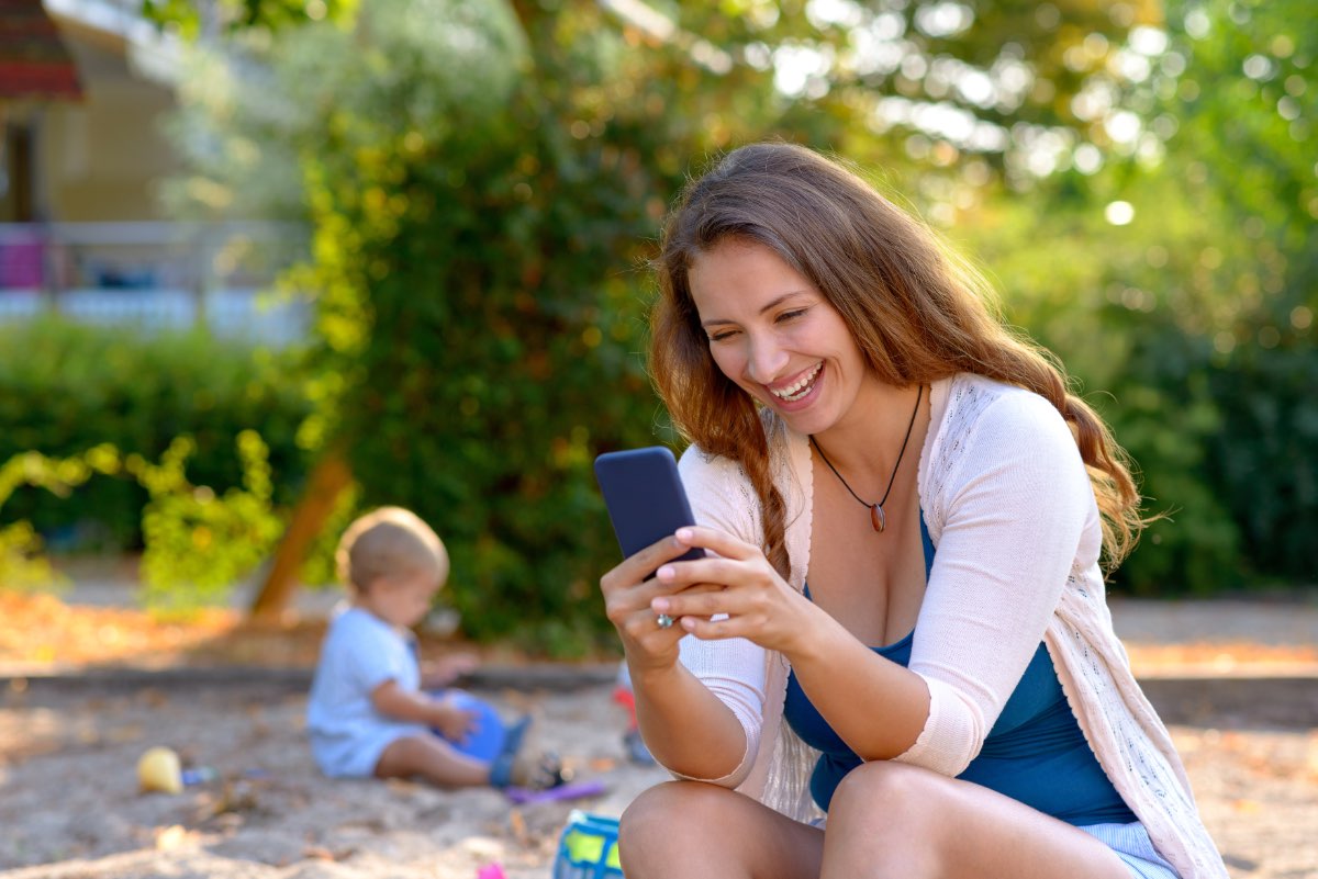 Eine Mutter sitzt auf einem Spielplatz und schaut auf ihr Handy.