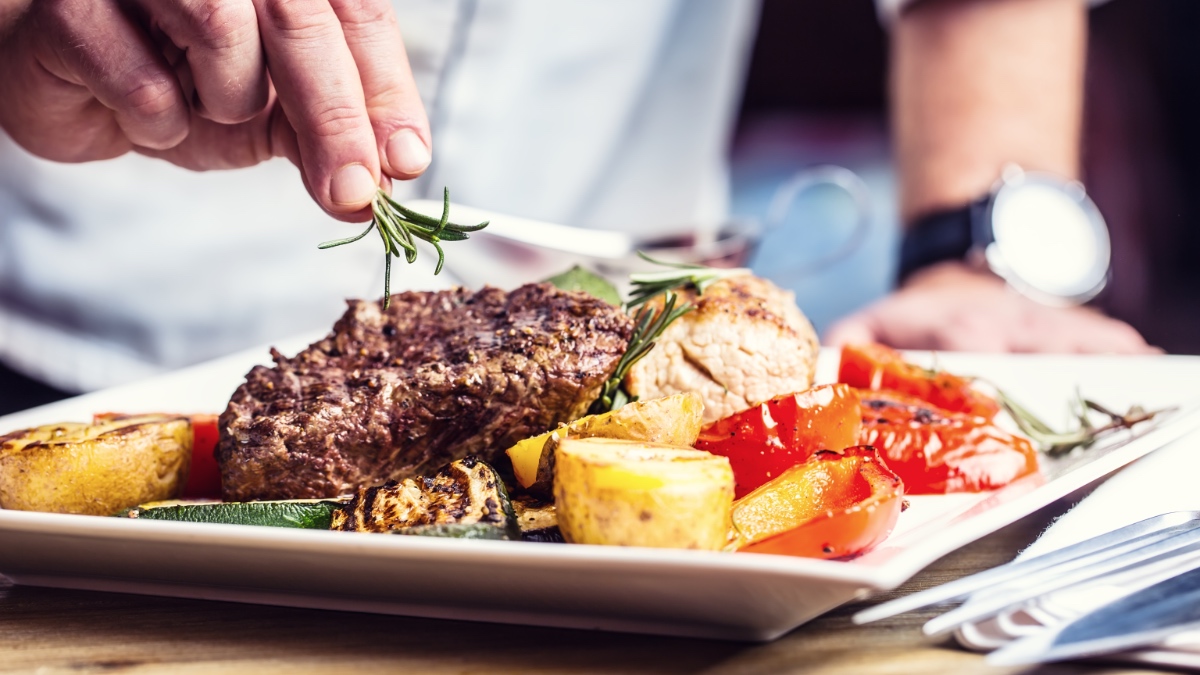 Ein Koch steht vor einem Teller mit Steak und Gemüse.