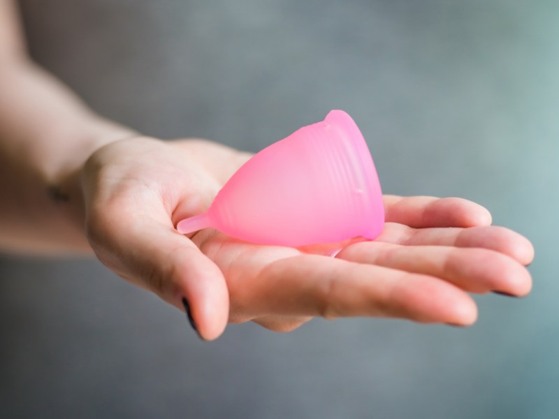 Eine Frau hält eine Menstruationstasse in der Hand.