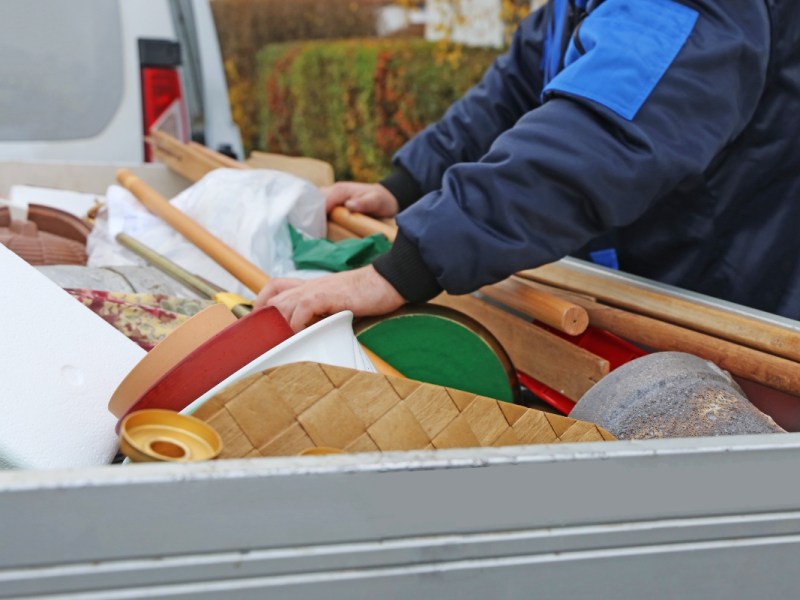 Eine Person in blauem Anzug durchsucht einen Container, der mit Sperrmüll gefüllt ist.