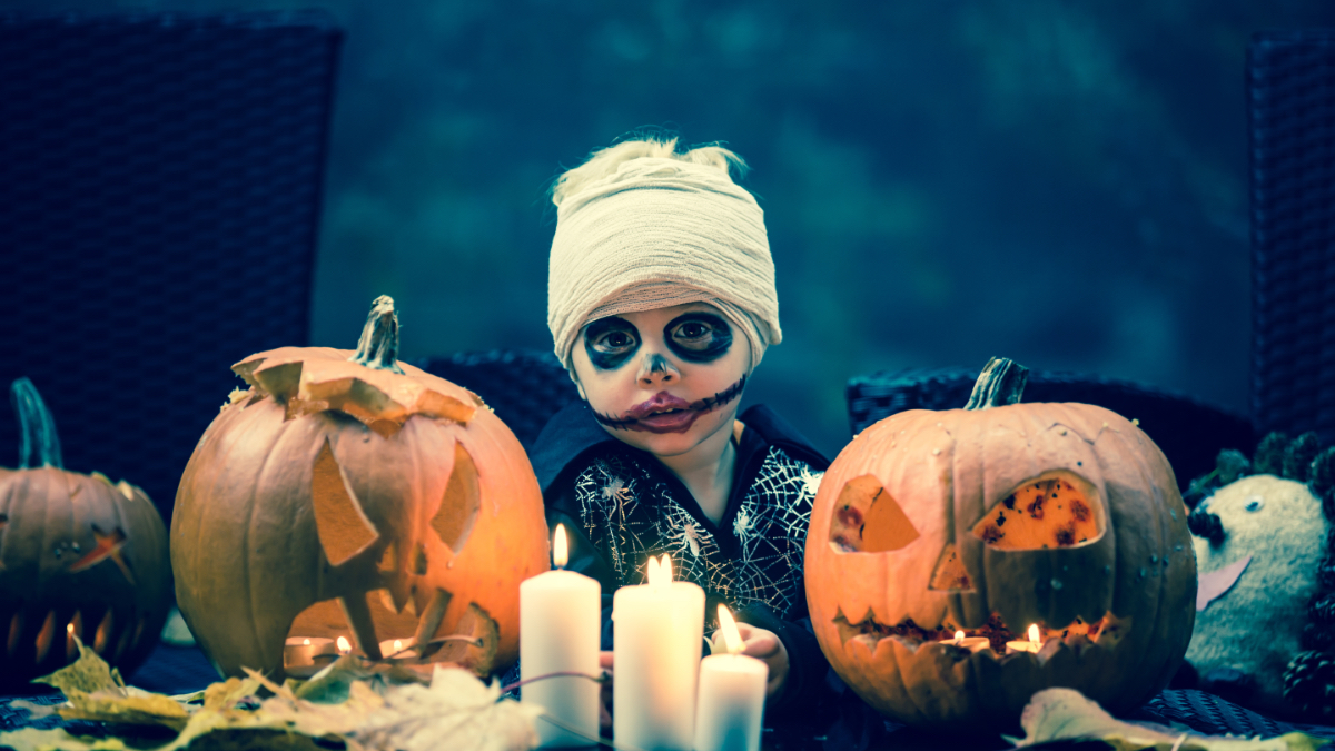 Ein Bild von einem Jungen in einem gruseligen Halloween-Kostüm, der vor Kürbis-Lampen sitzt.