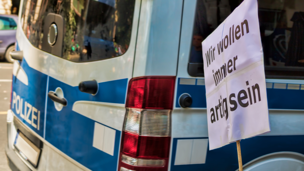 Ein Transparent an einem Stock, das vor einem Polizeiwagen steht.