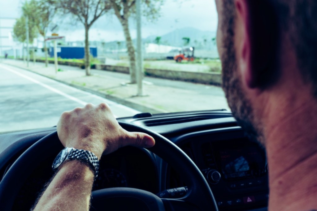 Ein Mann fährt Auto, mit der Hand auf dem Lenkrad.