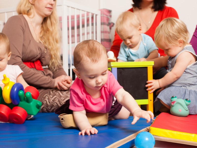 Eine Gruppe Kleinkinder werden in einer Kita von Erzieherinnen betreut.