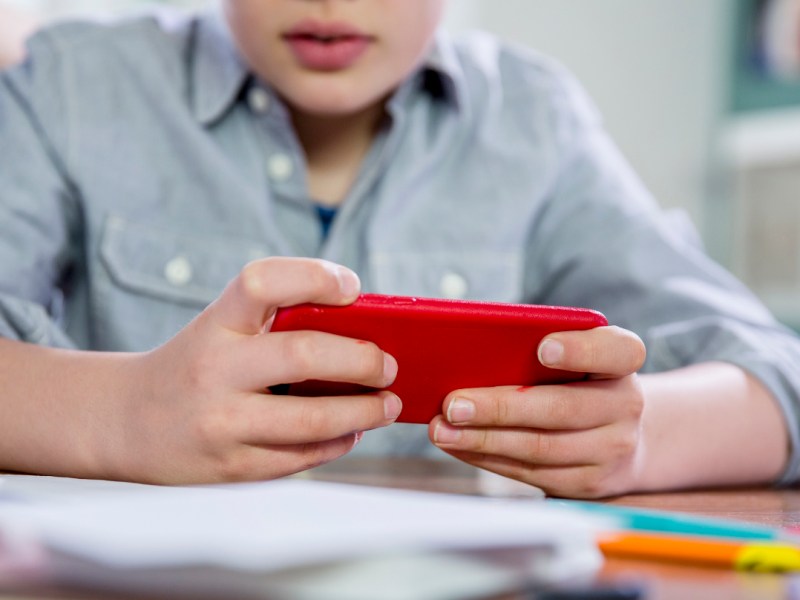 Ein blonder 10jähriger Junge spielt Videospiele auf seinem Handy.