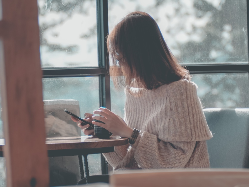 Eine junge Frau schaut in einem Café auf ihr Handy.