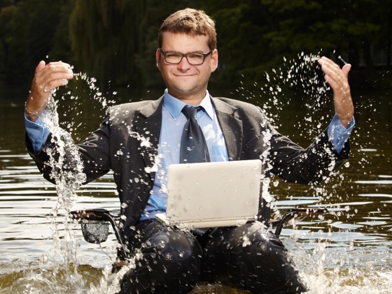 Ein Geschäftsmann sitzt mit Laptop im Wasser.