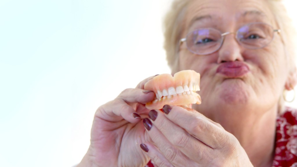 Eine Rentnerin hält ihr Gebiss in der Hand und schürzt die Lippen.