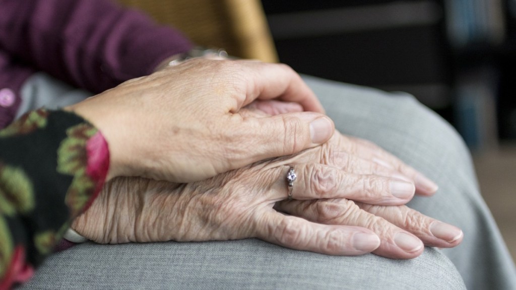 Eine Tochter hält die Hand ihrer alten Mutter.