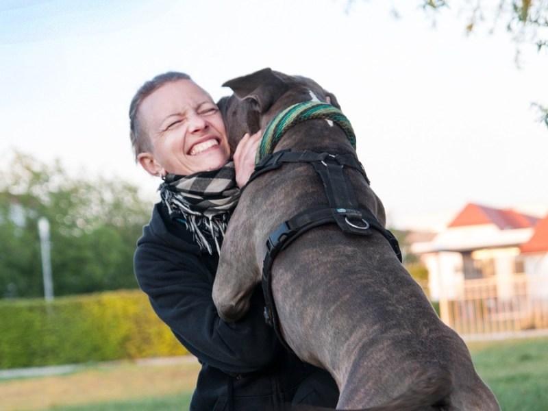 Eine Frau umarmt ihren Hund auf einer Wiese.