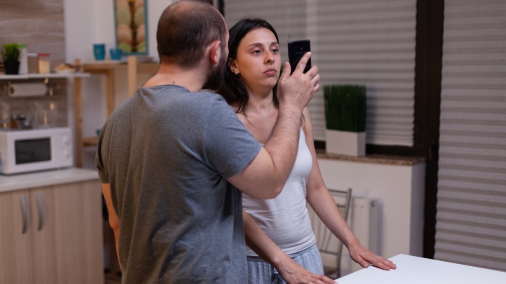 Ein Mann zeigt einer Frau sein Smartphone, auf den ein Nachweis zu sehen ist, dass sie ihn betrog.